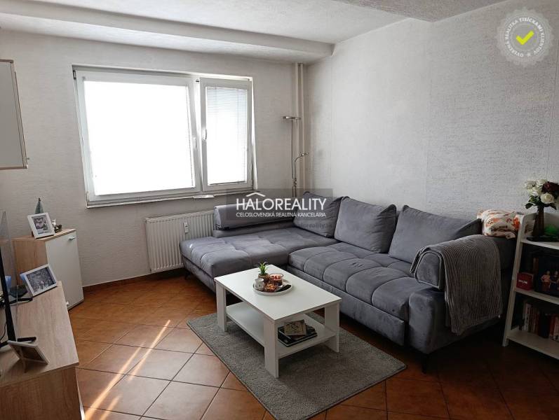 Wohnzimmer einer Zweizimmerwohnung mit Ecksofa und Tisch auf einem Boden mit Holzdekor.