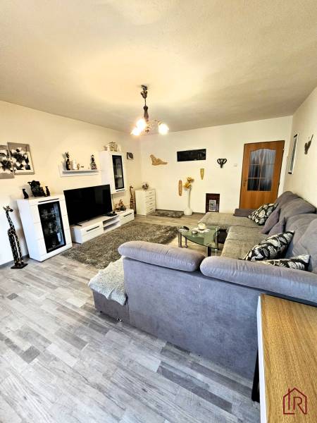 Wohnzimmer in einem Einfamilienhaus mit Holzboden, grauem Sofa und moderner Beleuchtung.