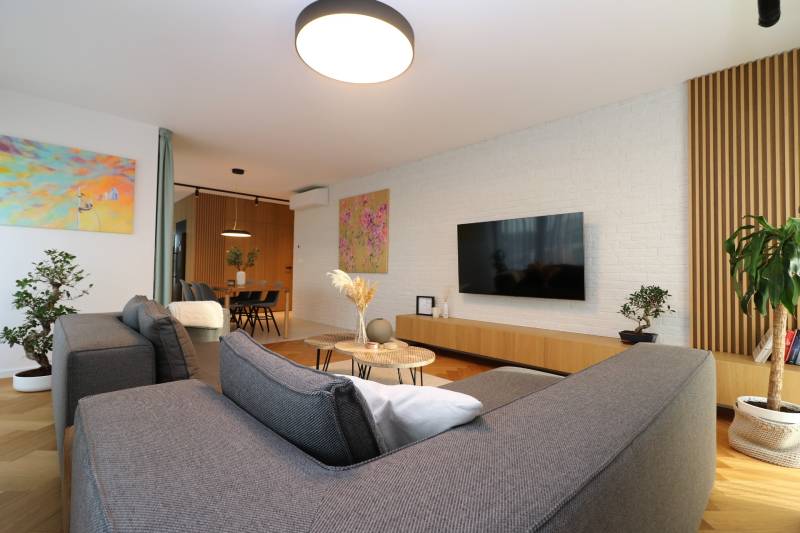 Wohnzimmer in einer Vierzimmerwohnung mit Holzboden, grauem Sofa und Pflanzen.