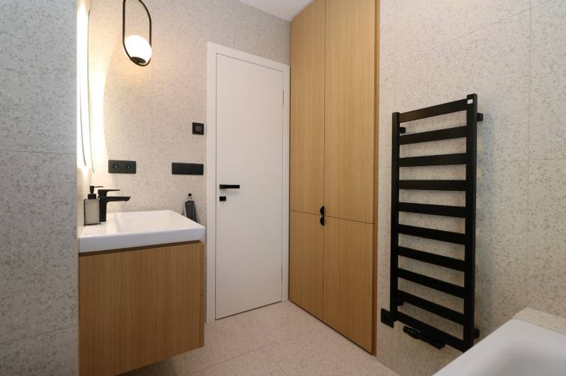 Badezimmer mit Schrank, weißem Waschbecken und schwarzem Leiterheizkörper in einer 4-Zimmer-Wohnung.