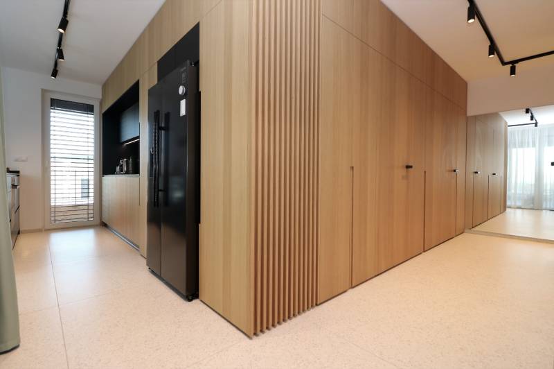 Küche in einer 4-Zimmer-Wohnung mit Holzdekor, einem schwarzen Kühlschrank und weißen Fliesen.