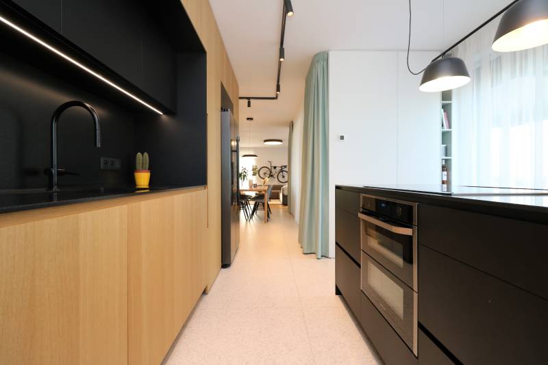 Küche in einer 4-Zimmer-Wohnung mit Holzelementen und schwarzen Accessoires.