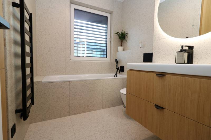 Badezimmer in einer 4-Zimmer-Wohnung mit Badewanne, Waschbecken und Holzdekor des Schranks.