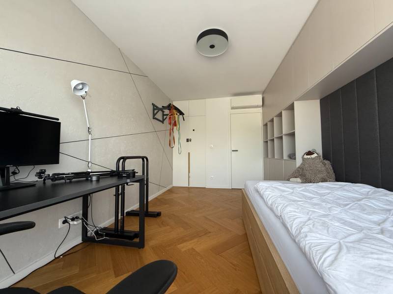 Ein Zimmer in einer 4-Zimmer-Wohnung mit einem Bett, einem Tisch und einem Boden in Holzoptik.