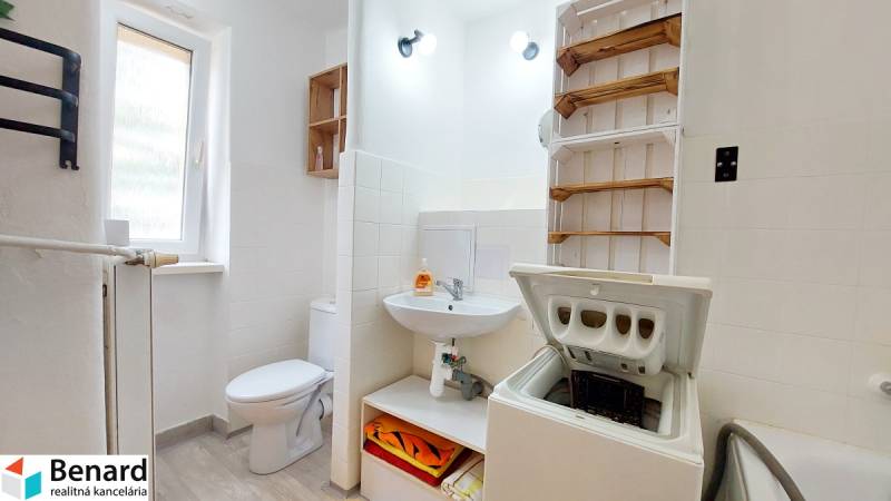 Badezimmer in einer 2-Zimmer-Wohnung mit Waschmaschine, Sanitäranlage und Regal für Handtücher.