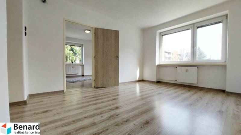 Zweizimmerwohnung mit Holzboden, großem Fenster und weißen Wänden.