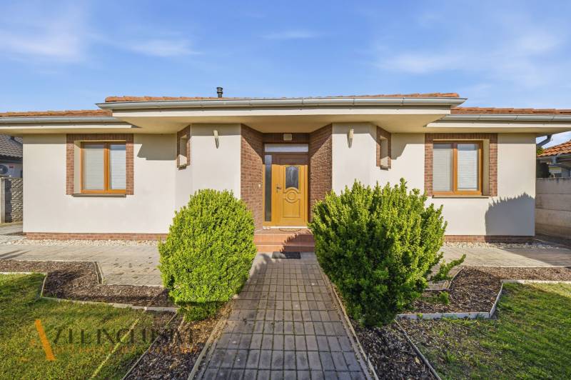 Ein Einfamilienhaus in Kútniky mit Strauchbepflanzung, weißer Fassade und braunen Akzenten.