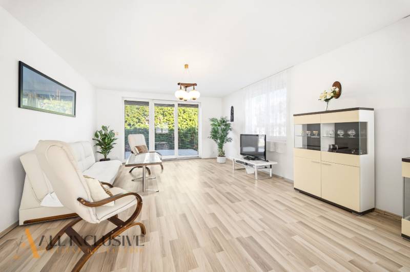 Helles Wohnzimmer mit Holzboden, Sofa, Sessel und Fernseher.