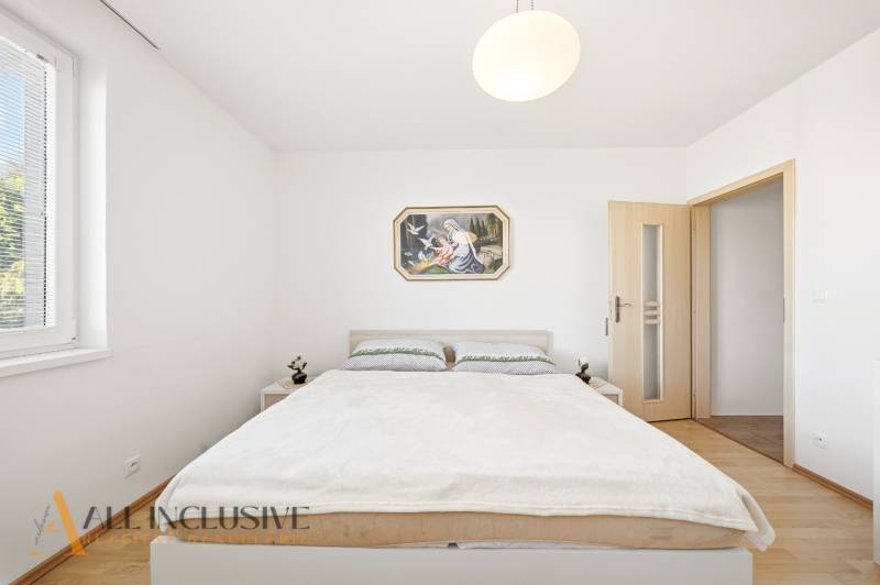 Ein Schlafzimmer in einem Einfamilienhaus mit einfacher Einrichtung und einem Boden in Holzoptik.