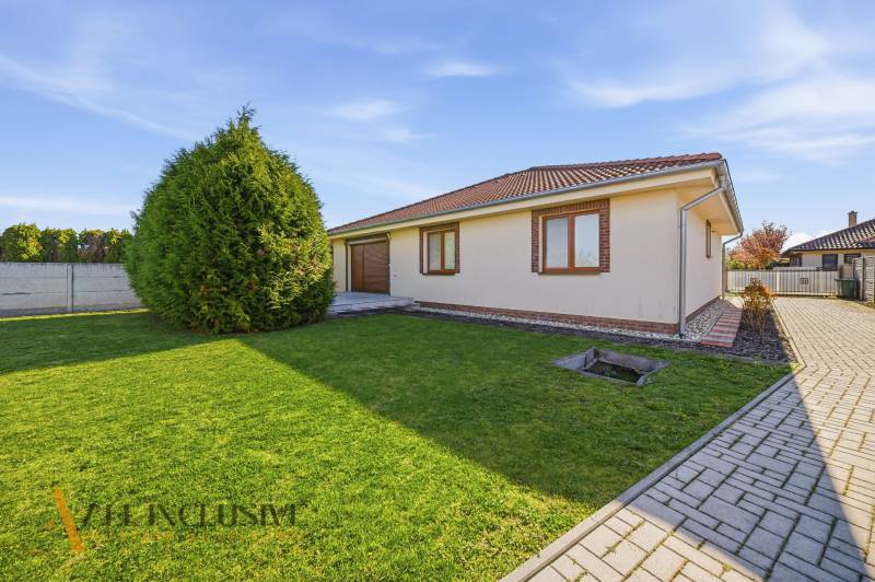 Ein Einfamilienhaus in Kútniky mit Rasen, Bäumen und Pflastersteinen.