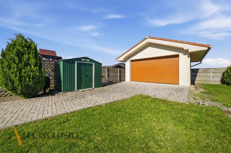Garage mit Holztor in einem Einfamilienhaus in Kútniky, mit Rasen und Gehweg.