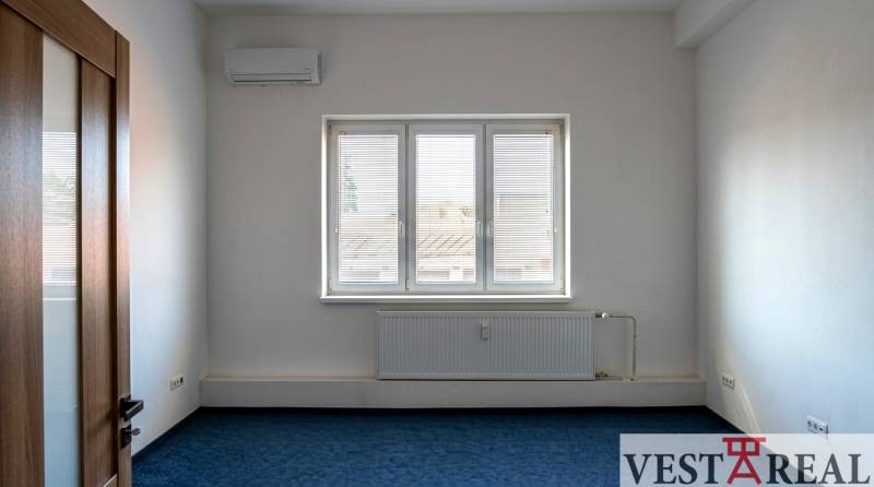Ein Zimmer mit Klimaanlage und Fenster in Büros, blauer Teppichboden, weiße Wände.