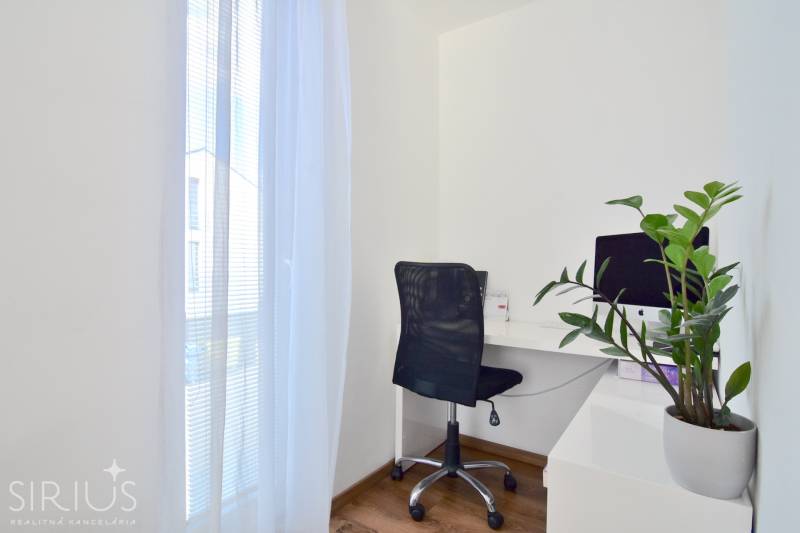 Arbeitsbereich mit Computer, schwarzem Stuhl und Pflanze auf einem Boden mit Holzdekor.