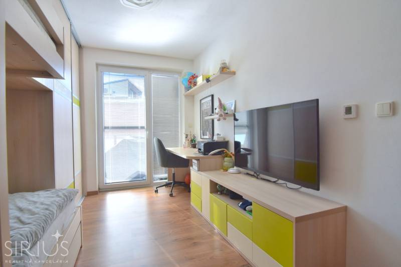 Ein Zimmer mit einem Boden in Holzoptik, einem Schreibtisch und einem Fernseher in einer 3-Zimmer-Wohnung.