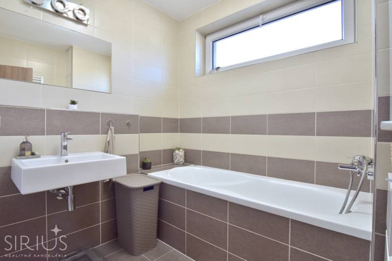 Badezimmer mit Badewanne und Waschbecken in einer 3-Zimmer-Wohnung mit beigen Fliesen.