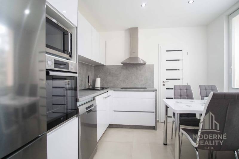 Küche in einer 2-Zimmer-Wohnung mit glänzenden Geräten, grauen Wänden und einem Esstisch.