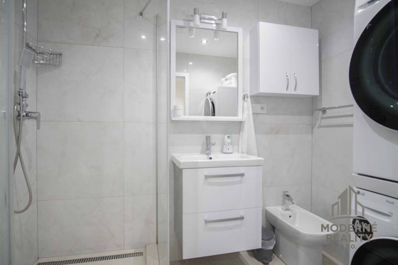 Badezimmer in einer 2-Zimmer-Wohnung mit Waschbecken, Duschkabine und Waschmaschine.