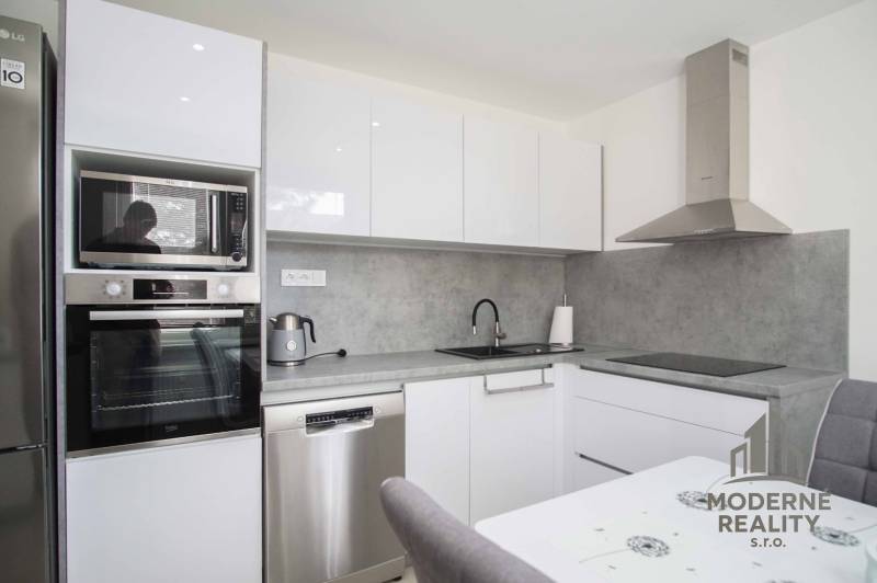 Moderne Küche mit weißen Schränken in einer 2-Zimmer-Wohnung, ausgestattet mit Geräten und Dunstabzugshaube.