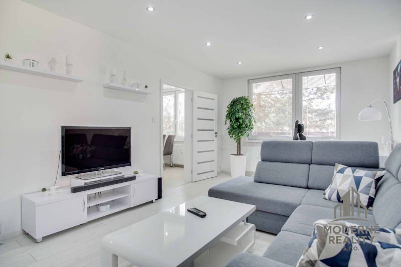 Wohnzimmer in einer Zweizimmerwohnung mit Fernseher, grauem Sofa und weißen Möbeln.