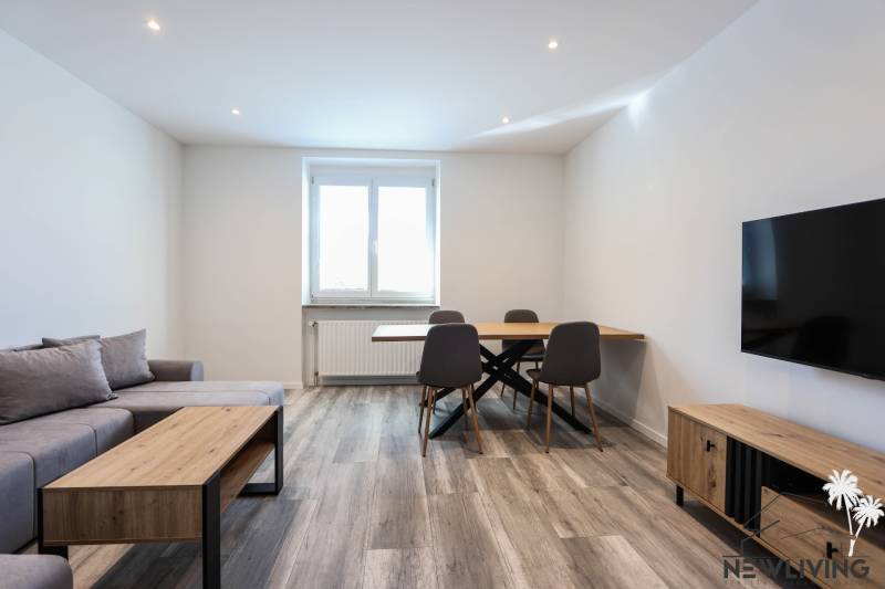 Wohnzimmer mit Holzboden, Sofa, Esstisch und Fernseher in einer 3-Zimmer-Wohnung.