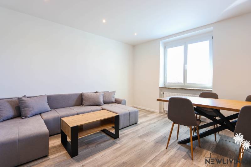 Wohnzimmer mit Ecksofa, Esstisch und Holzboden.