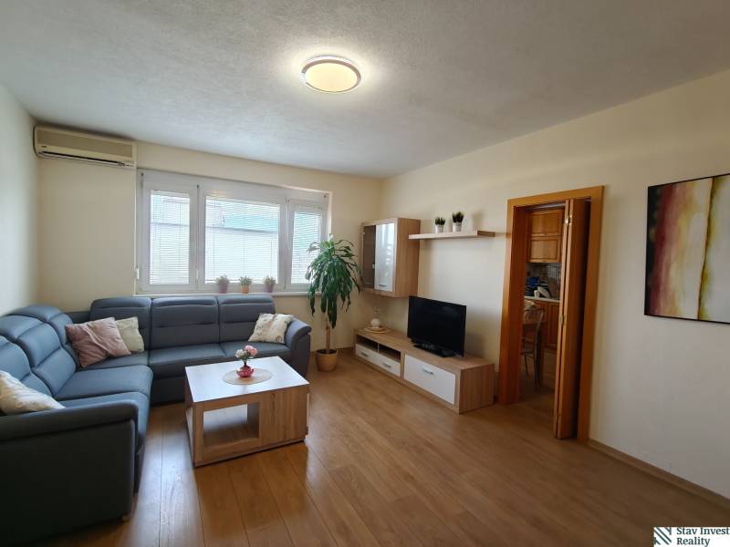 Helles Wohnzimmer mit einem blauen Sofa in einer 3-Zimmer-Wohnung, Boden mit Holzdekor.