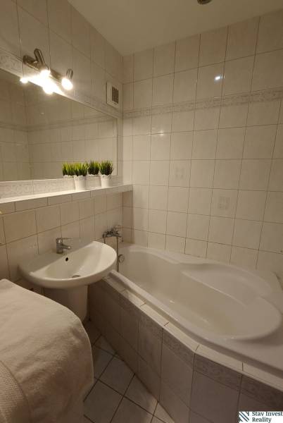Badezimmer mit Badewanne und Waschbecken in einer 3-Zimmer-Wohnung, weiße Fliesen und Dekorationen.