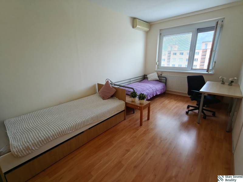 Ein Zimmer in einer 3-Zimmer-Wohnung mit zwei Betten, einem Schreibtisch und einem Boden mit Holzdekor.