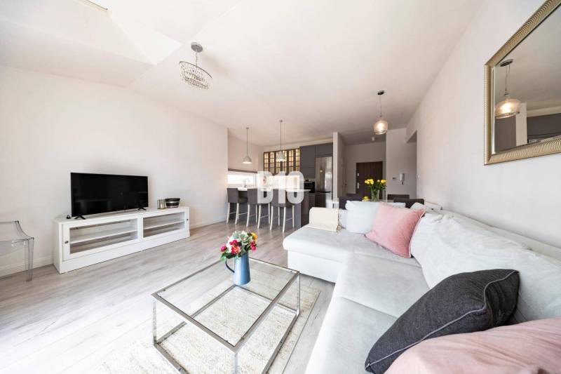 Wohnzimmer in einer 3-Zimmer-Wohnung mit Holzboden, weißem Sofa und Fernseher.