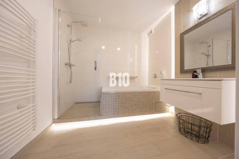 Badezimmer mit Badewanne, Dusche und Boden mit Holzdekor in einer 3-Zimmer-Wohnung.