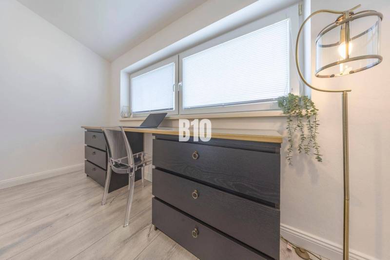 Ein Arbeitszimmer in einer 3-Zimmer-Wohnung mit Holzelementen, schwarzen Kommoden und einer Stehlampe.