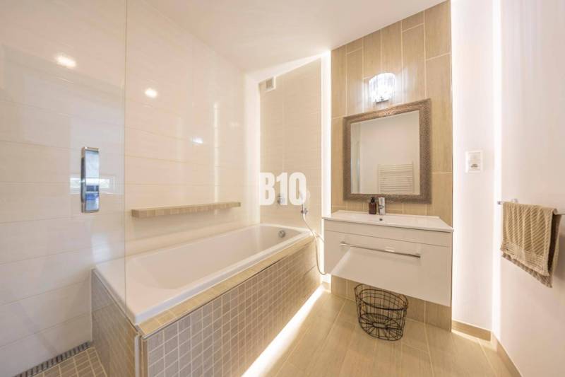 Badezimmer mit Badewanne, Waschbecken und Spiegel in einer 3-Zimmer-Wohnung mit Holzboden.