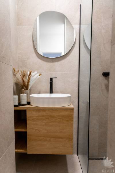 Badezimmer in einer 2-Zimmer-Wohnung mit einem Holzschrank, einem Spiegel und einem Waschbecken.