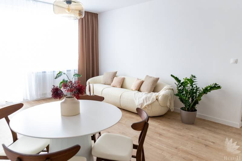 Innenraum einer 3-Zimmer-Wohnung mit cremefarbenem Sofa, Pflanze und Tisch auf einem Boden mit Holzdekor.