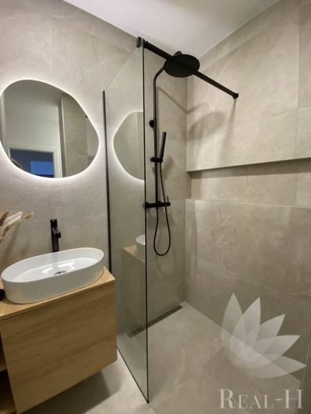 Badezimmer mit Waschbecken, Duschkabine und Spiegel in einer 3-Zimmer-Wohnung.