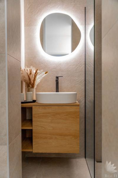 Badezimmer in einer 3-Zimmer-Wohnung mit einem Waschbecken auf einem Holzschrank und einem Spiegel mit Beleuchtung.