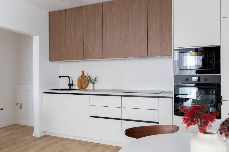 Küche in einer 2-Zimmer-Wohnung mit weißen Schränken und einem Boden in Holzoptik.