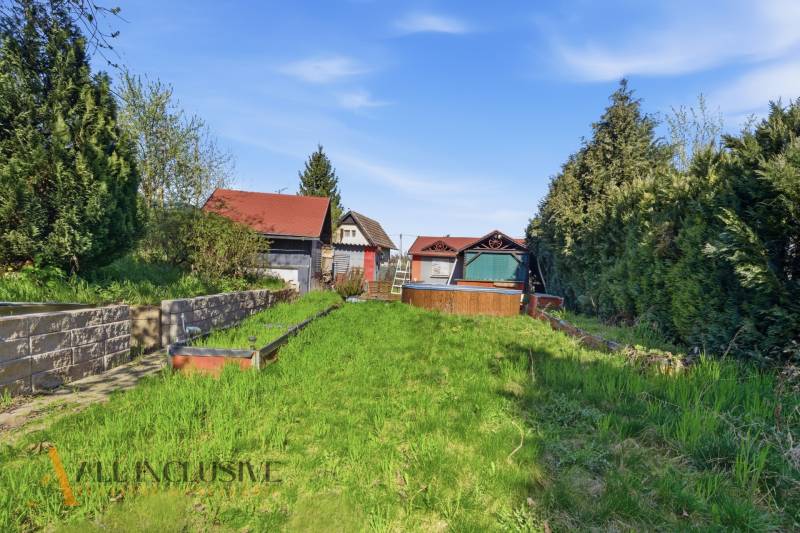 Gärten in Kráľová nad Váhom mit einem Häuschen, dichter Vegetation und Rasen unter blauem Himmel.