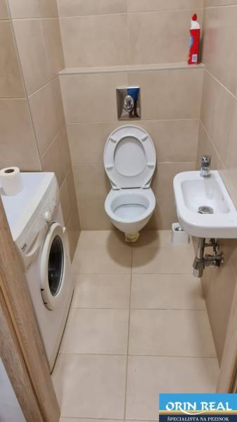 Badezimmer in einem Einzimmerapartment mit Toilette, Waschmaschine und kleinem Waschbecken.
