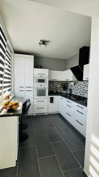 Küche in einer 3-Zimmer-Wohnung mit weißen Schränken, dunkler Arbeitsplatte und Obstdekor.