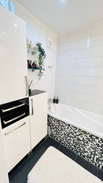 Badezimmer in einer 3-Zimmer-Wohnung mit weißer Badewanne, modernen Fliesen und Stauraum.