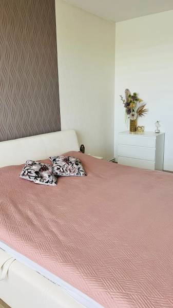 Schlafzimmer in einer 3-Zimmer-Wohnung mit Bett, dekorativen Kissen und ornamentaler Tapete.