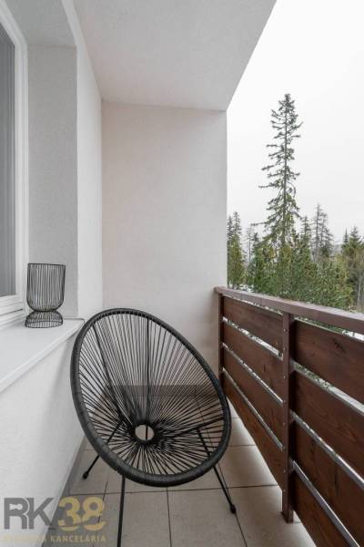 Balkon einer Ferienwohnung in Poprad mit einem schwarzen Sessel und Blick auf die Bäume.