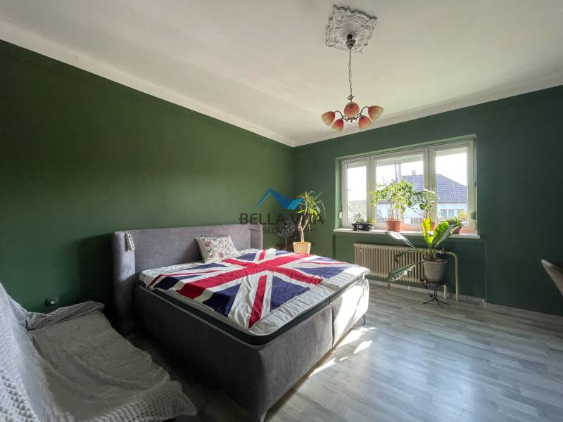 Spálňa v rodinnom dome s posteľou, zelenými stenami a podlahou s dreveným dekorom.