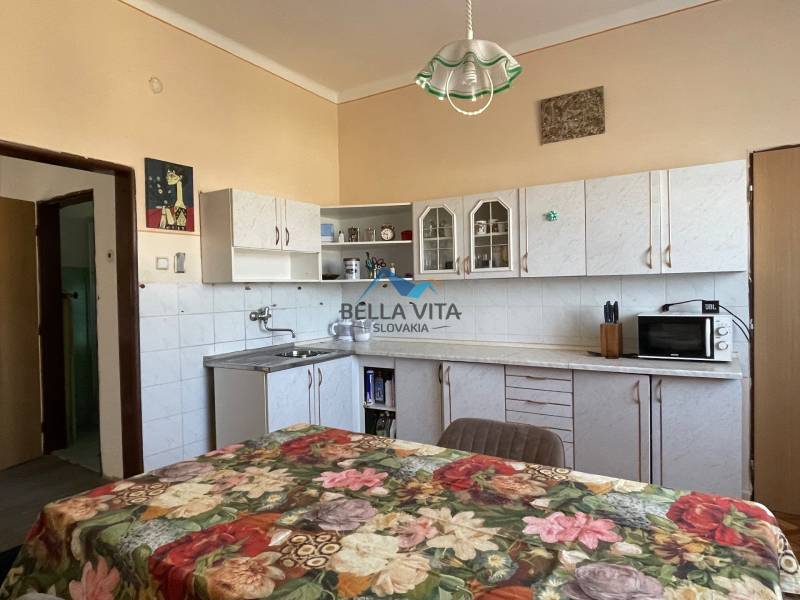 Kuchyňa v rodinnom dome s kvetinovým obrusom, bielymi skrinkami a farebnými stenami.