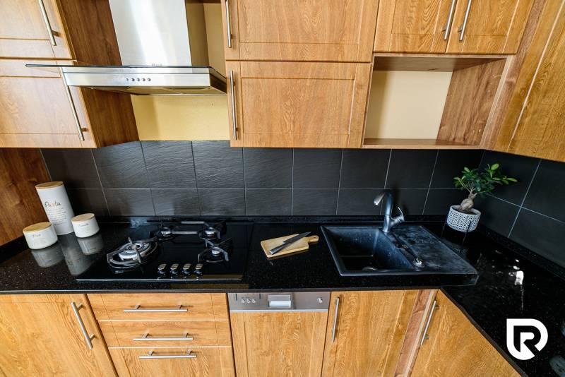 Küchenzeile in einer 2-Zimmer-Wohnung, mit Holzboden und dunklen Fliesen.