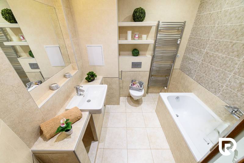 Badezimmer in einer 2-Zimmer-Wohnung mit Badewanne, Waschbecken, Spiegel und Handtuchhalter.