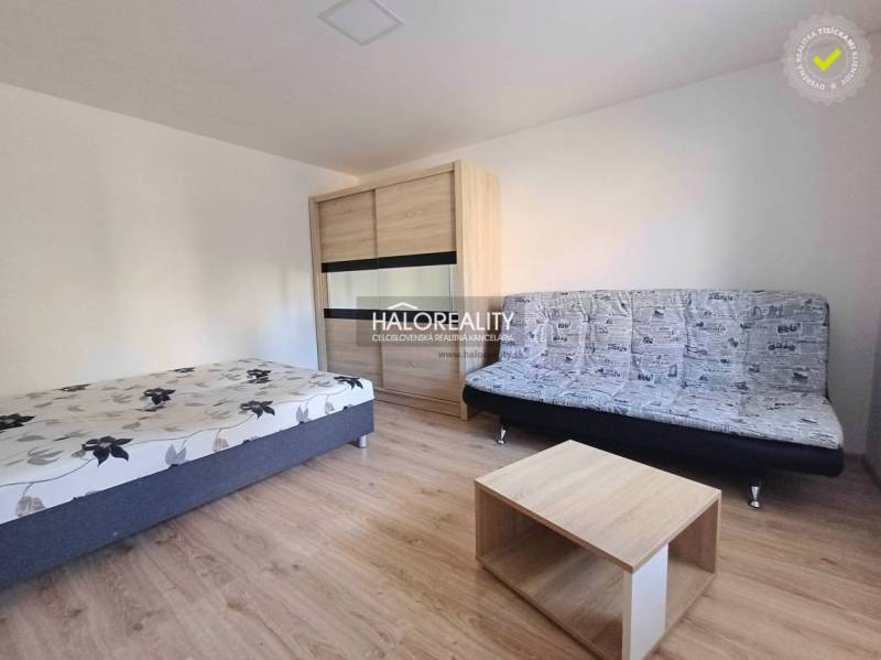 Innenraum einer 1-Zimmer-Wohnung mit Bett, Sofa und Boden in Holzoptik.
