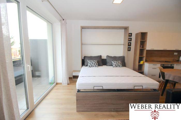 Schlafzimmer mit ausziehbarem Bett und Boden in Holzoptik in einer Einzimmerwohnung.
