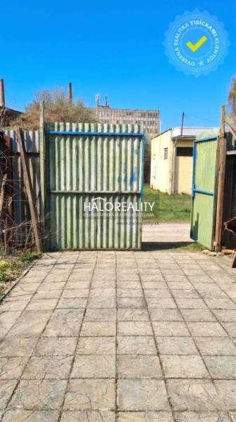 Der Hof bei der Hütte in Poltár mit einem Tor und Betonpflaster unter blauem Himmel.